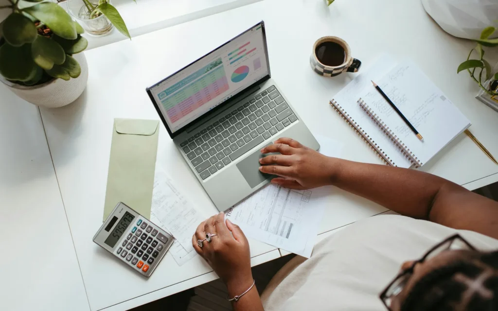 Small business owner planning a website budget at a bright desk with a laptop, calculator and coffee