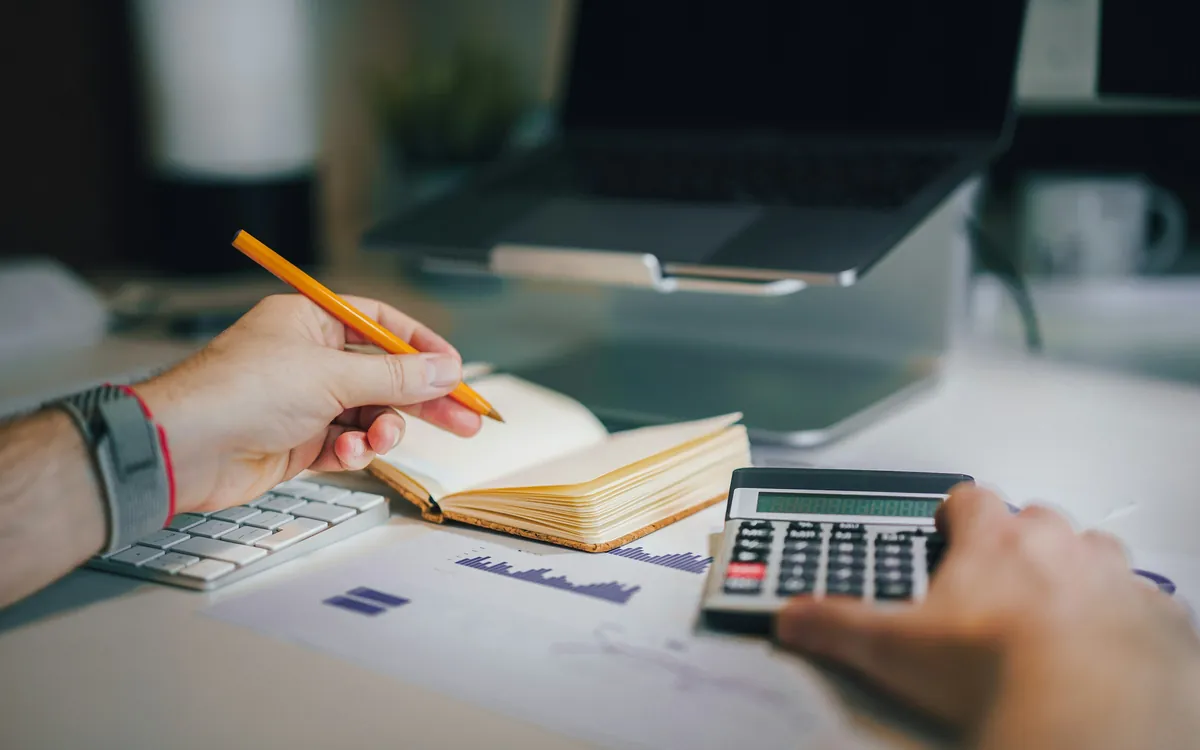 Hands working out a website budget with a calculator and a notebook next to a laptop - Small business website cost